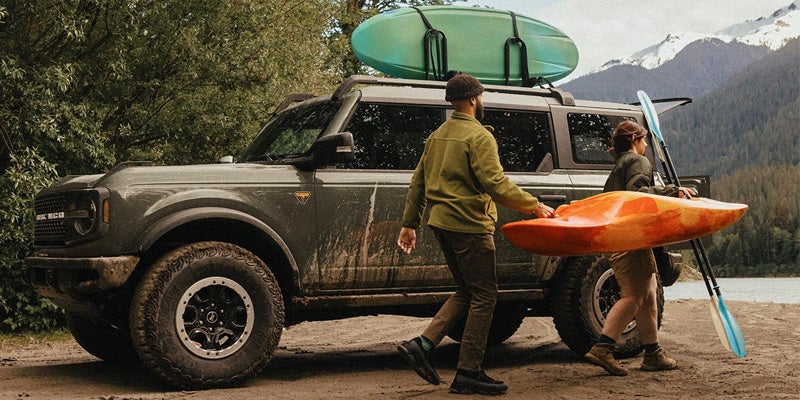 Ford Bronco parked by a lake as two people unload a kayak