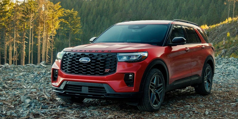 Red Ford Explorer ST parked on a rocky trail beside pine trees