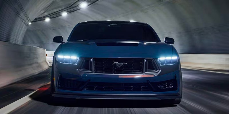 Front view of a blue-gray sports coupe driving through a tunnel, with bright LED headlights illuminated
