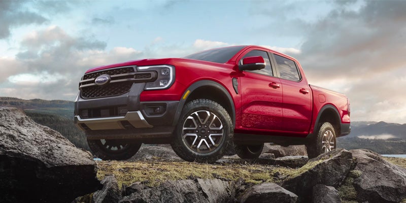 Red midsize pickup truck parked on rocky terrain, viewed from a low front three-quarter angle