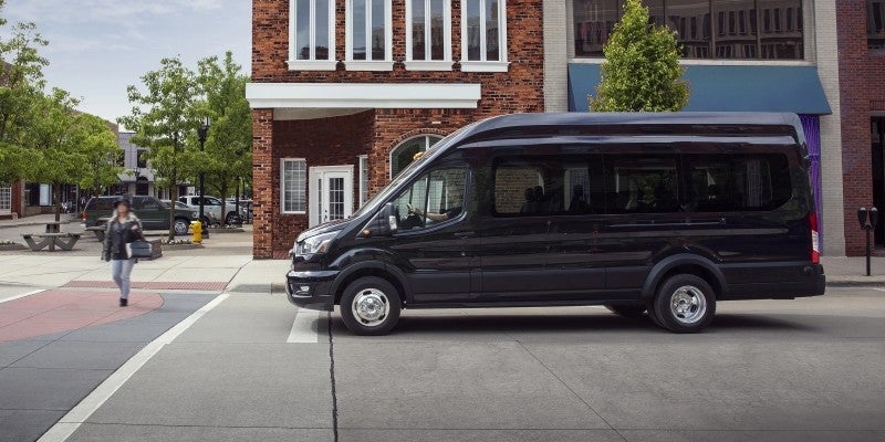 Black passenger van parked at a city intersection, viewed from the side in front of brick storefronts and a pedestrian crosswalk