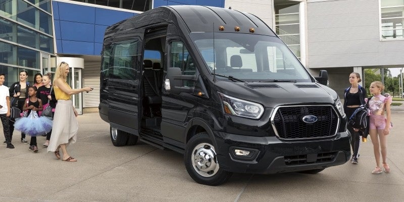 Black shuttle van with its sliding door open outside a modern building, as a group of people prepares to board