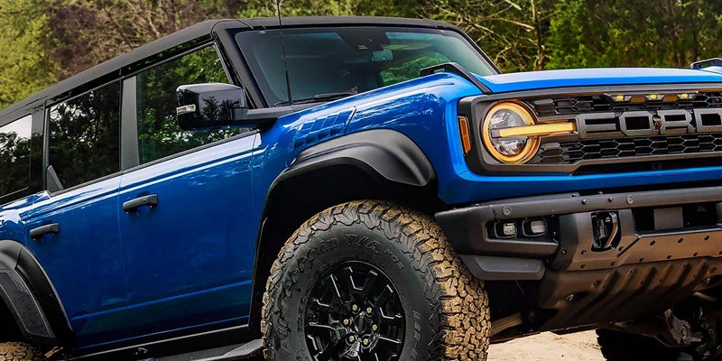 Blue off-road SUV shown from a close front three-quarter angle, featuring rugged all-terrain tires, black fender flares