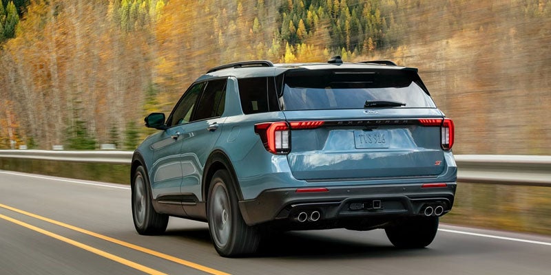 Rear view of a blue Ford Explorer ST driving on a highway, with autumn trees blurred in the background.