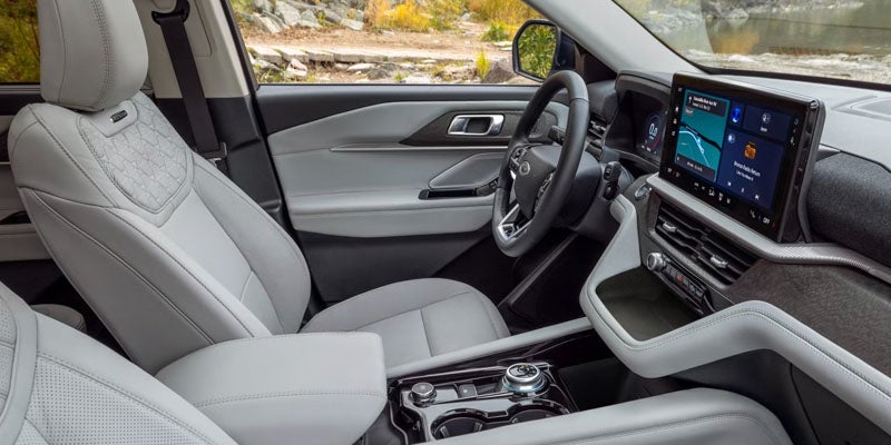 The spacious light gray interior of a modern car, featuring a large infotainment screen, and diamond-stitched seat accents.