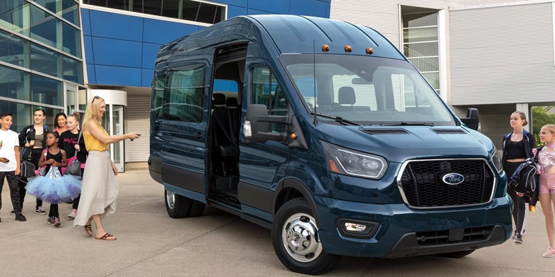 Dark blue high-roof shuttle van parked outside a modern building with the side sliding door open